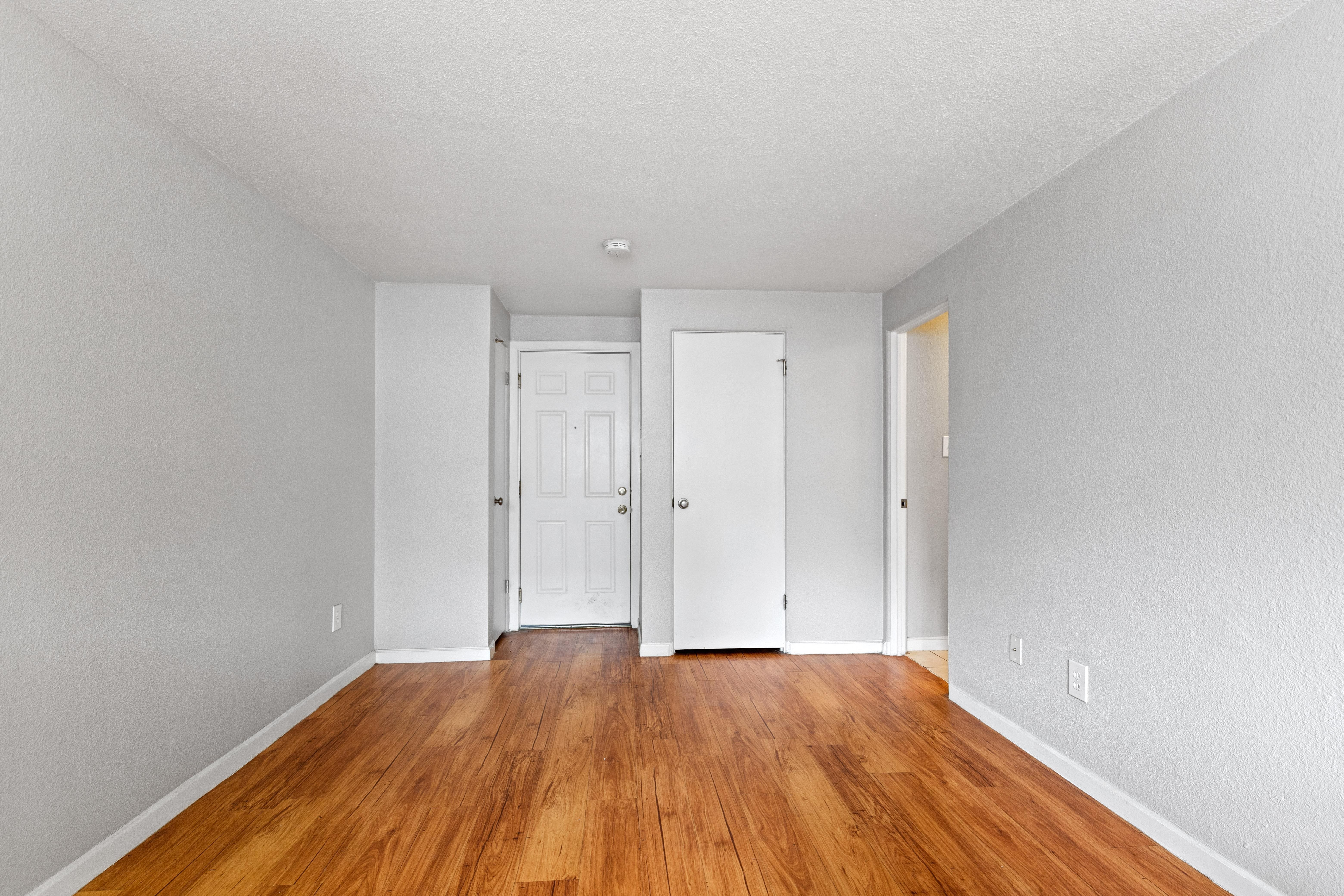 the living room of an apartment with wood floors and white walls